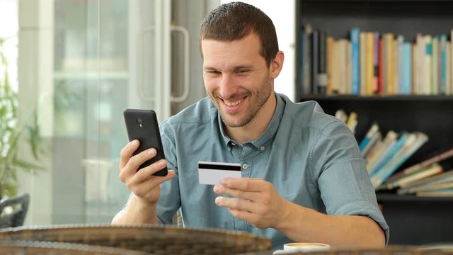 Happy man buying online with card and smart phone sitting in a coffee shop
