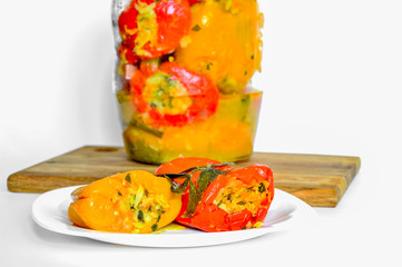 Stuffed vegetables pickled red and yellow peppers lie on a white plate on the background of a jar of peppers.