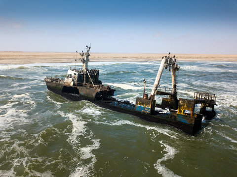 Abandoned and derelict old shipwreck Zeila at the Atlantic Coast near Swakopmund and famous Skeleton Coast in Namibia, Africa. Group of cormorants birds perching on rusted ship. Drone view.