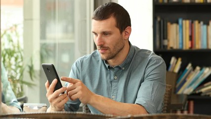 Serious man using a smart phone and finds funny content in a coffee shop