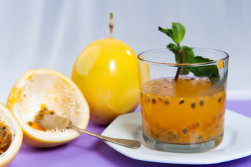 Passion fruit juice, in the foreground, focused. Passion fruit, in the background, blurred. Natural calming.Close view.Cassis color background.