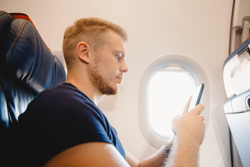 Obraz premium Man uses smart mobile phone in cabin airplane, concept Internet in air stratosphere