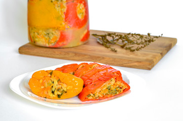 Sliced stuffed red and yellow whole peppers lie on a white plate close-up against a jar of peppers. White background, copy space.