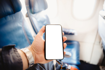 White screen mobile phone in cockpit of plane against background seats and portholes. Copy space