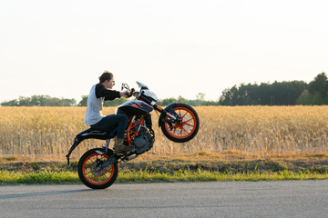 Plakat Teenage boy on a dirtbike motorcycle doing a wheelie at sunset