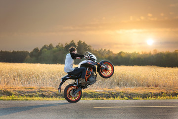 Teenage boy on a dirtbike motorcycle doing a wheelie at sunset