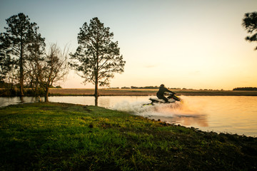Teenage boy man driving a personal watercraft outside on a lake pond at sunset