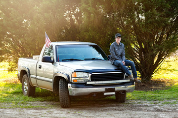happy teenage boy from the south sitting on the front of his pickup truck outside in a rural area. 