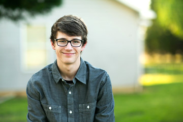 Teenage Boy with Glasses Outside on a spring day sitting outside of a house home smiling - obrazy, fototapety, plakaty