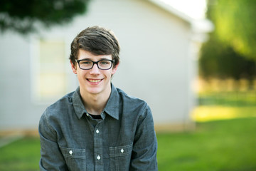 Teenage Boy with Glasses Outside on a spring day sitting outside of a house home smiling