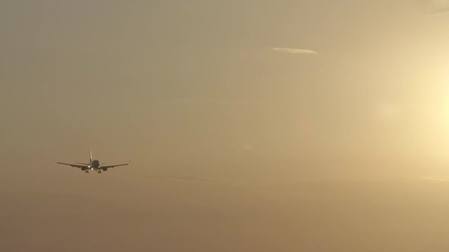 Silhouette of small jet airplane is landing in yellow sunset with wind