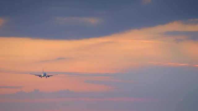 Silhouette of small jet airplane is landing in blue and purple sunset with clouds