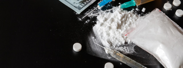 drug is a white powder, tablets, syringes sprinkled on a black table. Dangerous illegal business....