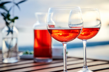 two glasses of rose wine with  olives against blue water on a pier..