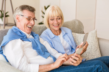 Happy mature couple watching funny videos on phone