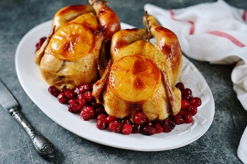 Two whole roasted chicken with cranberries and orange slices.