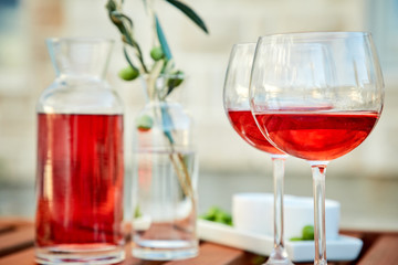 two glasses of rose wine with  olives against blue water on a pier..