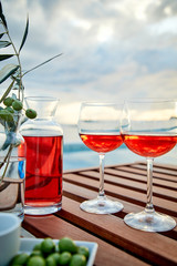 two glasses of rose wine with  olives against blue water on a pier..