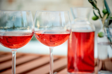 two glasses of rose wine with  olives against blue water on a pier..