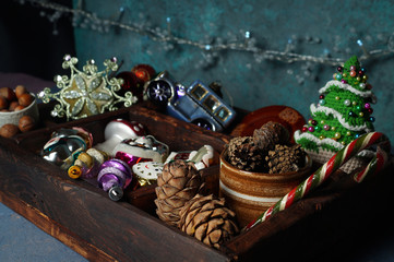 Wooden box with New Year's toys, pine, spruce, cedar cones, knitted Christmas tree, glass machine, openwork snowflake-Christmas tree toy, nuts in a ceramic cup and a garland.