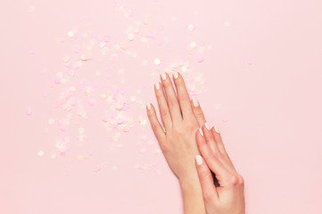 Obraz na płótnie Canvas Stylish fashionable female manicure in pastel colors. Hands of young girl on pink background with festive confetti. Minimalist manicure trend. Flat lay, top view, copy space for your text