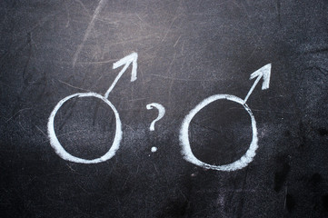 On a black chalkboard are drawn male signs of affiliation with a question mark between them. Gender affiliation