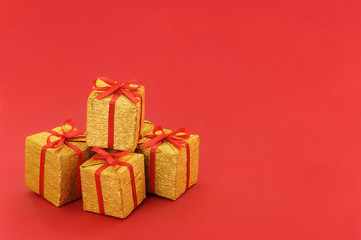 Stack of small golden gift box with red ribbon and bow on red background, with empty place for text on the right. Close up.