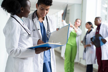 a pair of doctors, mixed race. Young people in white coats, doctors, smiling, are holding medical...