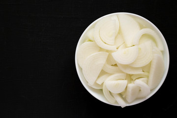 Chopped raw white onions in a white bowl on a black background, top view. Flat lay, overhead, from above. Copy space.