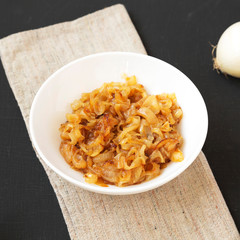 Homemade caramelized onions on a white plate on a black surface, low angle view. Close-up.