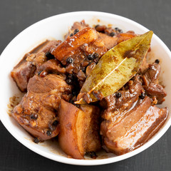 Homemade Filipino Adobo Pork in a white bowl on a black background, low angle view. Close-up.