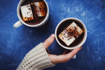 Flat lay of woman's hands in sweater and two cups of cocoa or hot chocolate with homemade vegan marshmallow