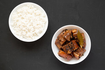 Homemade Filipino Adobo Pork with rice on a black wooden background, top view. Flat lay, overhead, from above.