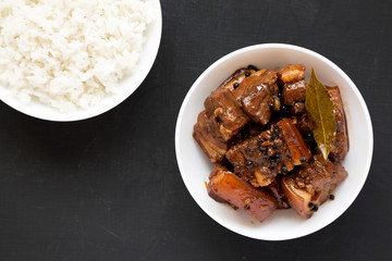 Homemade Filipino Adobo Pork with rice on a black wooden surface, top view. Flat lay, overhead, from above.