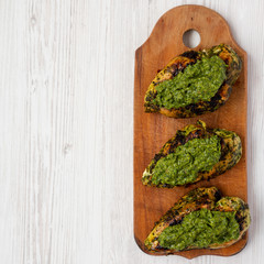 Grilled chimichurri chicken breast on a rustic wooden board on a white wooden table, top view. Flat lay, overhead, from above. Space for text.