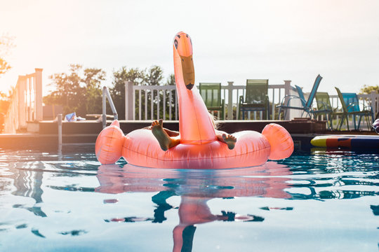 Low section of person sitting on flamingo swim ring during sunset