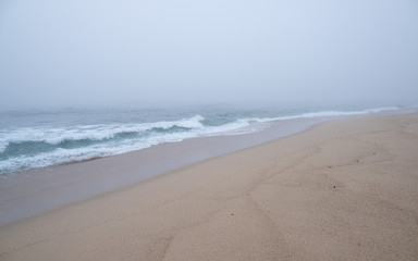 Thick, dense fog over the ocean as waves break on the empty, sandy beach.