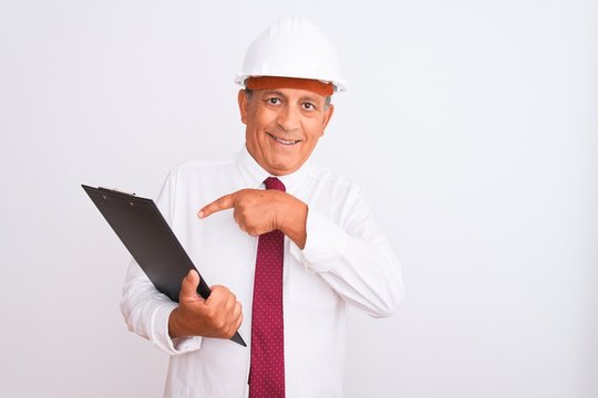 Senior architect man wearing security helmet holding clipboard over isolated white background very happy pointing with hand and finger