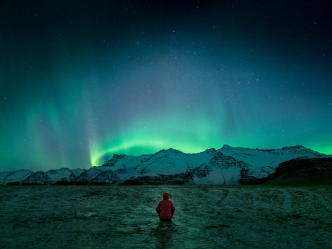 Person wearing red hoodie standing in front of northern lights