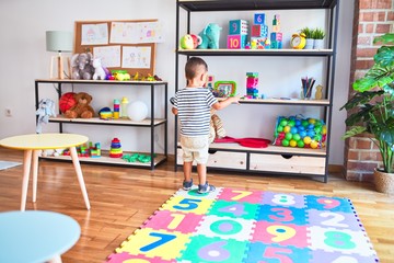 Beautiful toddler boy holding magnifying glass at kindergarten