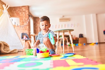 Beautiful toddler boy sitting on puzzle playing meals with plastic plates, fruits and vegetables at...