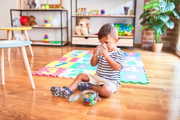 Beautiful toddler boy drinking glass of water at kindergarten