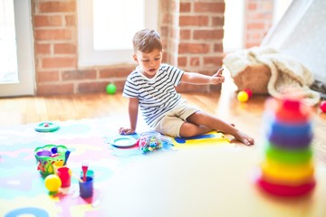 Beautiful toddler boy sitting on puzzle playing meals with plastic plates, fruits and vegetables at...