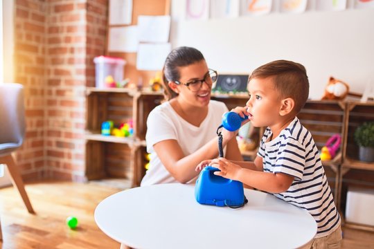 Beautiful teacher and toddler boy playing with vintage blue phone at kindergarten