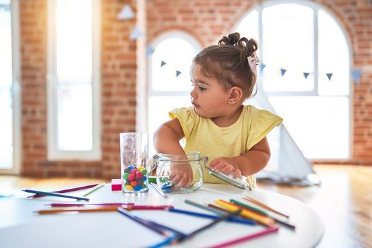 Beautiful toddler standing playing with chocolate colored balls on the table at kindergarten