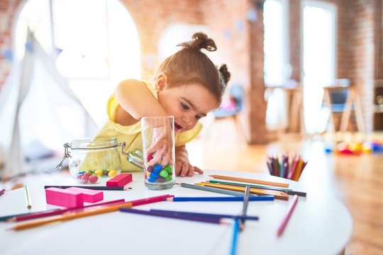 Beautiful toddler standing playing with chocolate colored balls on the table at kindergarten