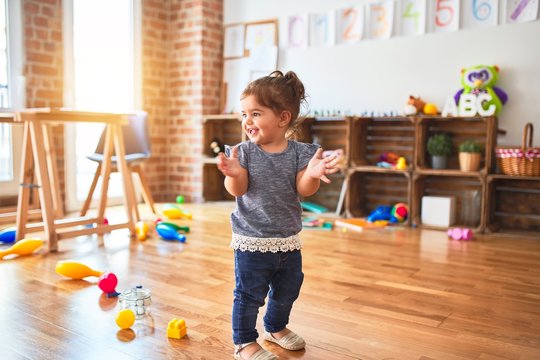 Beautiful toddler applauding  standing around lots of toys at kindergarten