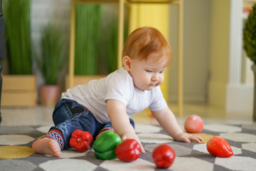 Fototapeta premium chubby child with red hair plays with vegetables