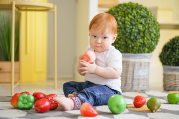 Fototapeta na wymiar chubby child with red hair plays with vegetables