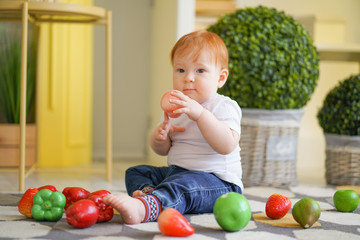 Fototapeta premium chubby fatty baby child with plus size body and red hair plays with vegetables and like his diet on room background